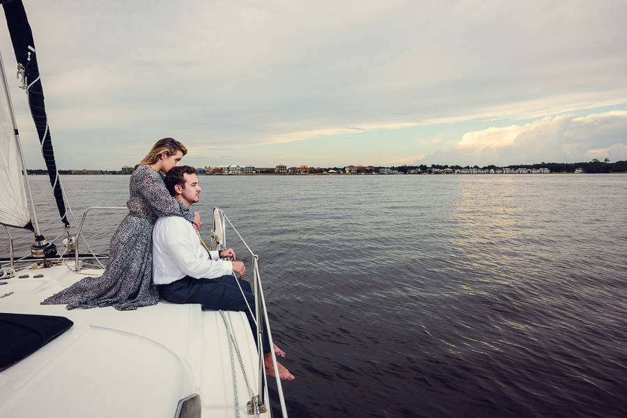 Newlyweds hugging and looking out over the water on a sailboat, Epic Pensacola Sunset Sailing, Lazzat Photography