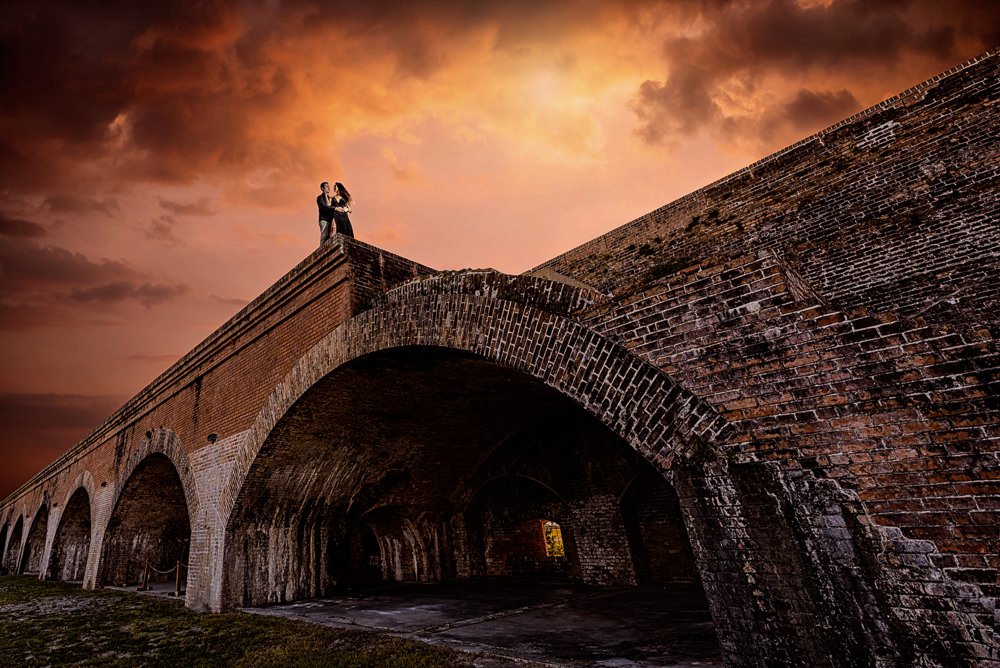 Timber+Alec at the edge of the wall with epic sunset and arches during their Ft. Pickens Sunset Engagement Session, Timber+Alec, Ft. Pickens Sunset Engagement Session, Pensacola engagement photographer, Pensacola engagement photo session, Pensacola engagement photos, Pensacola engagement photography, Lazzat Photography