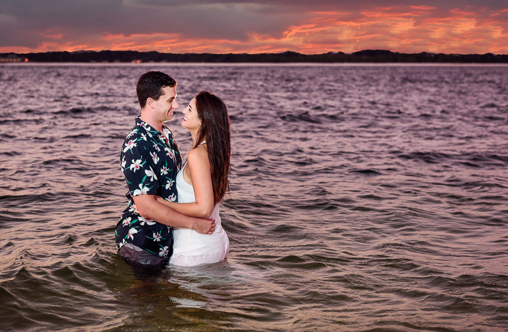 Timber+Alec standing in the water facing each other and smiling with an epic sunset during their Ft. Pickens Sunset Engagement Session, Timber+Alec, Ft. Pickens Sunset Engagement Session, Pensacola engagement photographer, Pensacola engagement photo session, Pensacola engagement photos, Pensacola engagement photography, Lazzat Photography